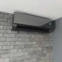 Szary klimatyzator LG zamontowany na ścianie z dekoracyjnej cegły, z widocznym wyświetlaczem temperatury 18 stopni Celsjusza.