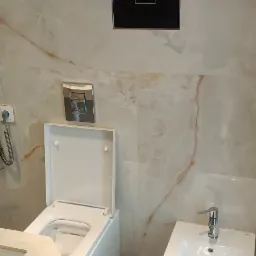 Nowoczesna łazienka z wiszącą toaletą z deską wolnoopadającą, bidetem i marmurowymi płytkami na ścianach oraz podłodze z szarymi żyłami, elektroniczny panel sterowania nad toaletą.