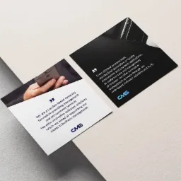 Dwie kwadratowe ulotki z informacjami o firmie CMS, jedna z dłonią trzymającą smartfon, druga z tekstem o oprogramowaniu i narzędziach, leżące na teksturowanym podłożu.