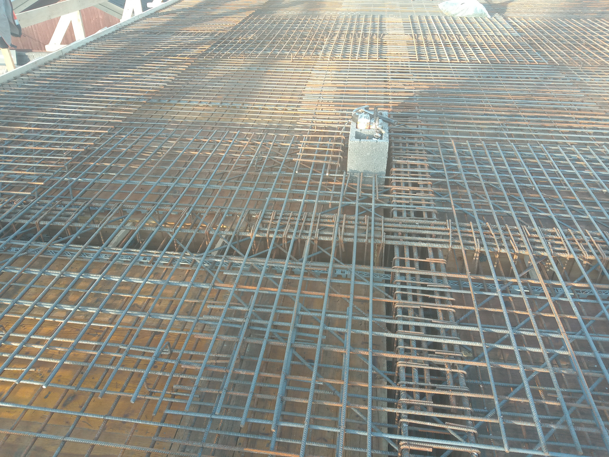Zbrojenie stropu z siatki stalowej na deskowaniu, z betonową kostką dystansową pośrodku kadru, widoczne elementy drewniane konstrukcji.