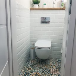 Usługi Remontowo Budowlane ,, BODEX '' - Zbigniew Boho - Kompaktowa łazienka z wiszącą toaletą, białe kafelki typu metro, wzorzysta podłoga w stylu patchwork, drewniana półka z roślinami i dyfuzorem zapachowym.
