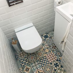 Usługi Remontowo Budowlane ,, BODEX '' - Zbigniew Boho - Wysoki kąt widzenia na białą toaletę i umywalkę w małej łazience z białą cegłą na ścianach i dekoracyjnymi płytkami podłogowymi w stylu patchwork.