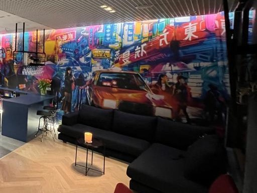 Wnętrze biura z fotorealistyczną tapetą przedstawiającą futurystyczne miasto azjatyckie, ciemnoszara sofa z małym stolikiem i świecą, parkiet ułożony w jodełkę.