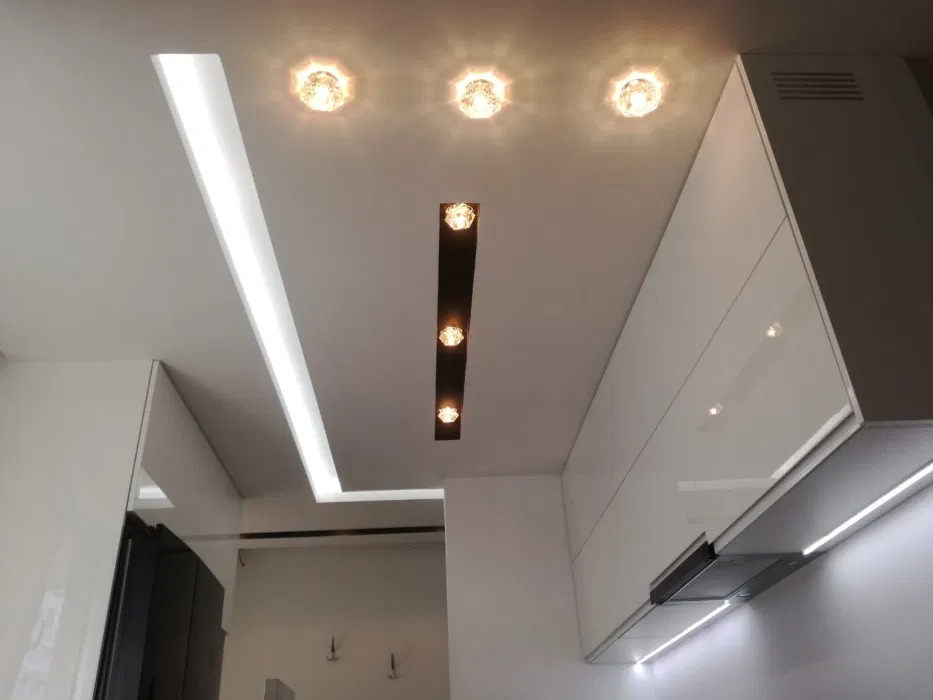 Nowoczesny sufit podwieszany z oświetleniem LED liniowym i punktowym w kuchni z białymi szafkami na wysoki połysk.