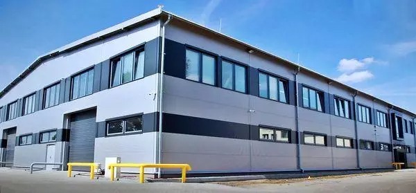 Nowoczesny budynek magazynowy z szaro-czarną elewacją i licznymi oknami, oświetlony słonecznym światłem.