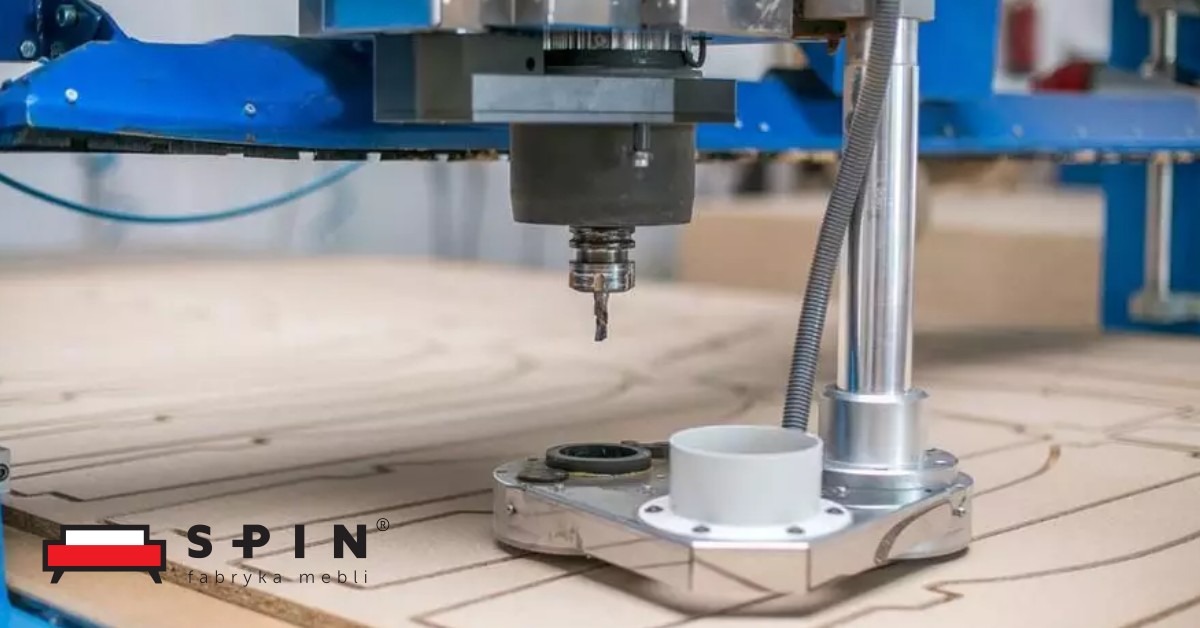 Frezarka CNC w trakcie obróbki płyty meblowej z widocznym logo producenta mebli w lewym dolnym rogu.