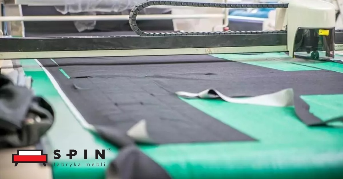 Automatyczny ploter tnący precyzyjnie wycina elementy z ciemnej tkaniny na zielonym stole, przygotowane do produkcji mebli tapicerowanych.