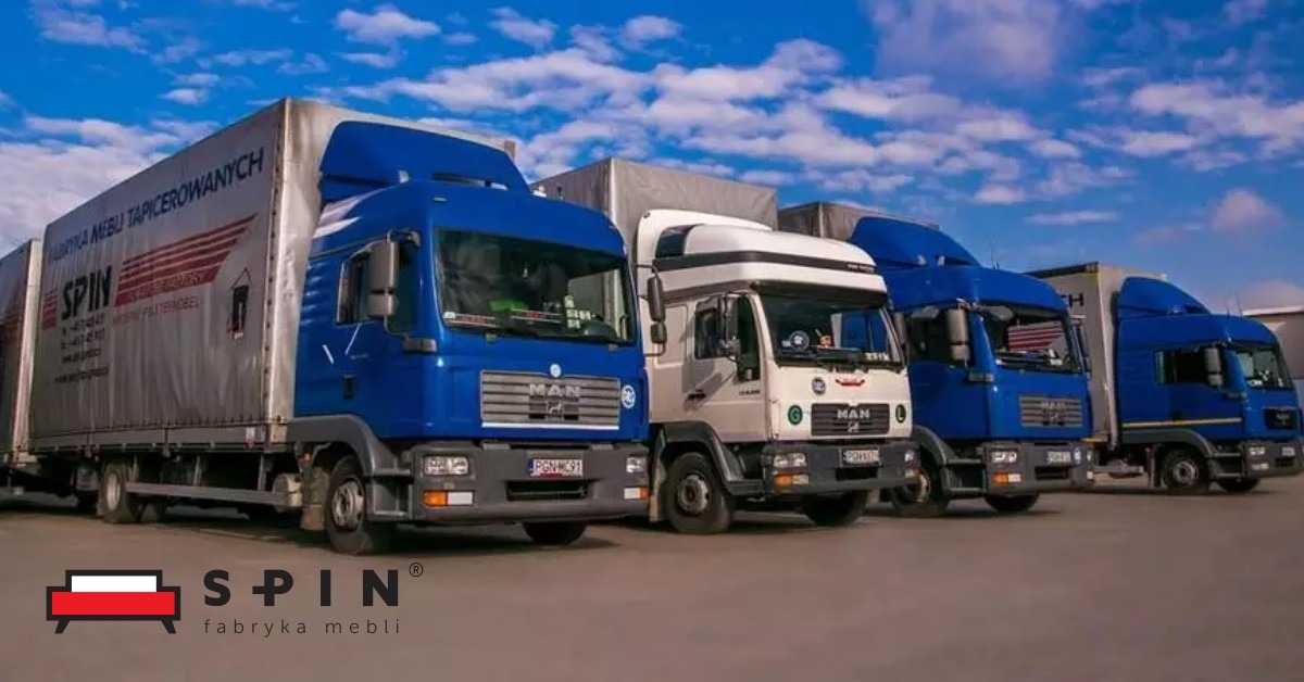 Flota ciężarówek z logo producenta mebli tapicerowanych na tle błękitnego nieba z chmurami.