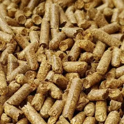 Stos brązowych, cylindrycznych peletów z biomasy drzewnej, z widoczną strukturą włókien drzewnych, wypełniających całą przestrzeń kadru.