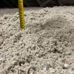 Luźno ułożona warstwa szarej wełny celulozowej na poddaszu, z żółtą miarką wskazującą grubość izolacji na około 40 cm.