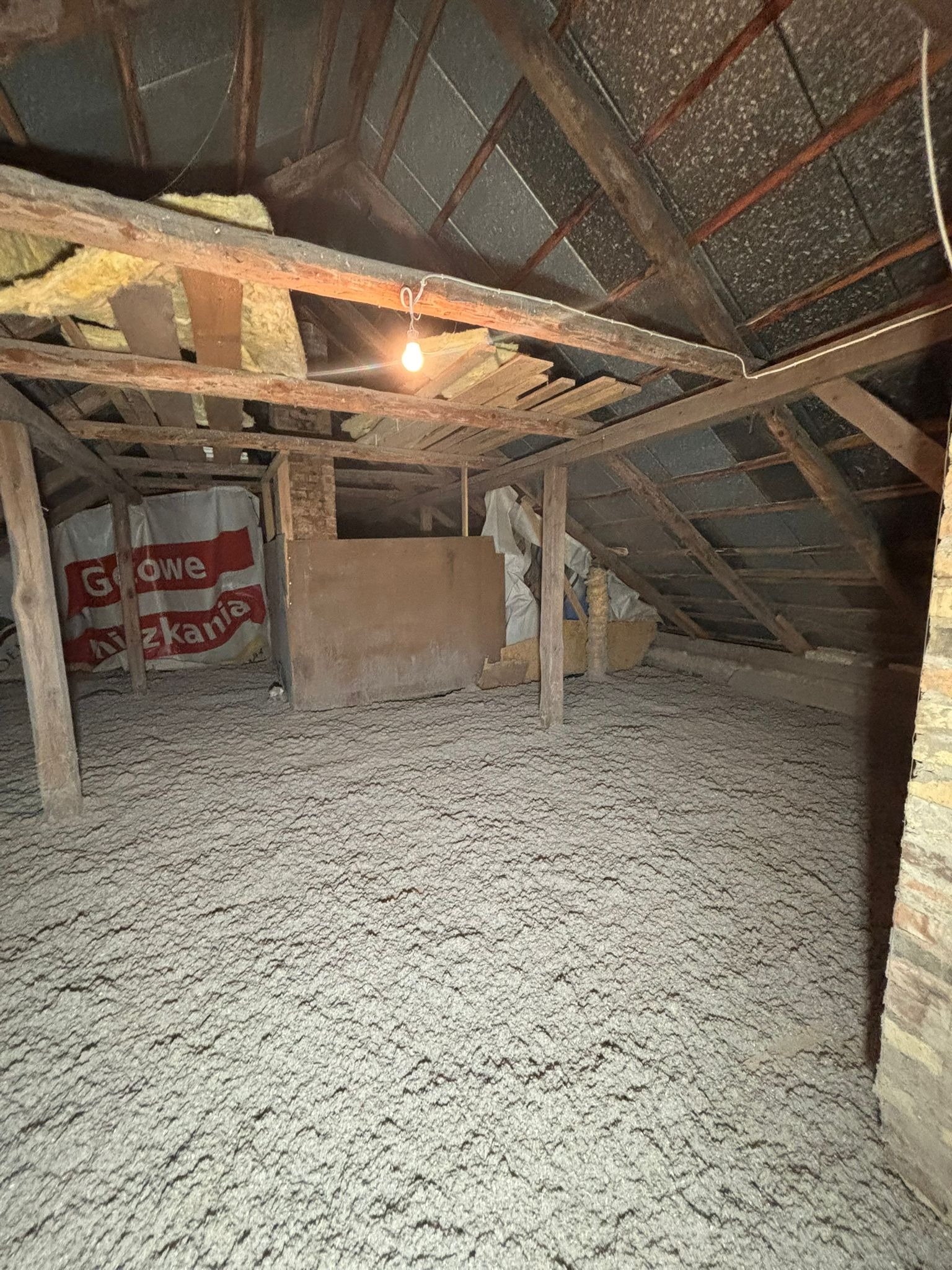 Poddasze po izolacji w Zambrowie. Widoczna warstwa wełny mineralnej, drewniana konstrukcja dachu i wisząca żarówka. Izolacja wykonana z dbałością o detale.
