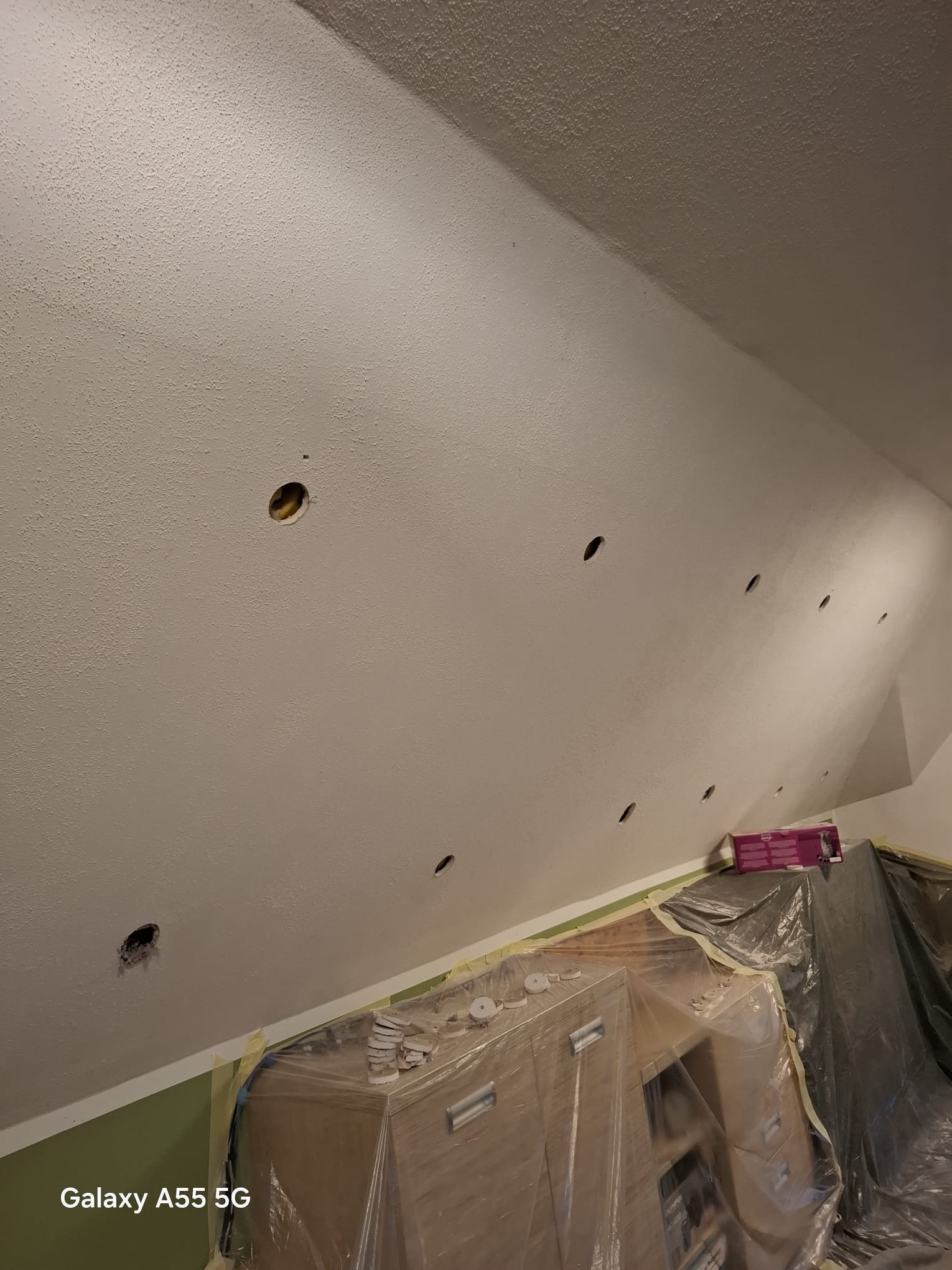 Poddasze z wywierconymi otworami pod ocieplenie, zabezpieczone meble folią malarską. Widoczne ślady po wierceniu i przygotowania do wdmuchiwania izolacji.