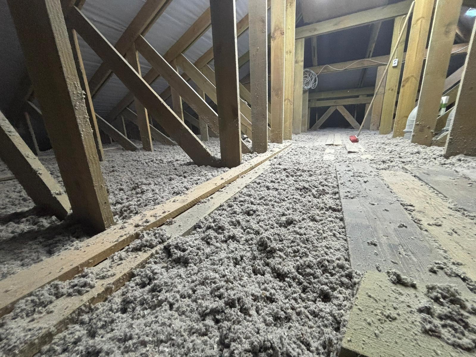 Ocieplone poddasze wełną mineralną, widoczne drewniane elementy konstrukcji dachu i podłogi. Izolacja równomiernie rozłożona, tworząca grubą warstwę.