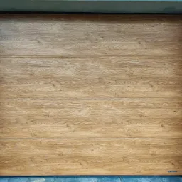 Zamknięta brama garażowa segmentowa z paneli imitujących jasne drewno dębowe, widoczna od wewnątrz, z czarną ramą i logo producenta w prawym dolnym rogu.