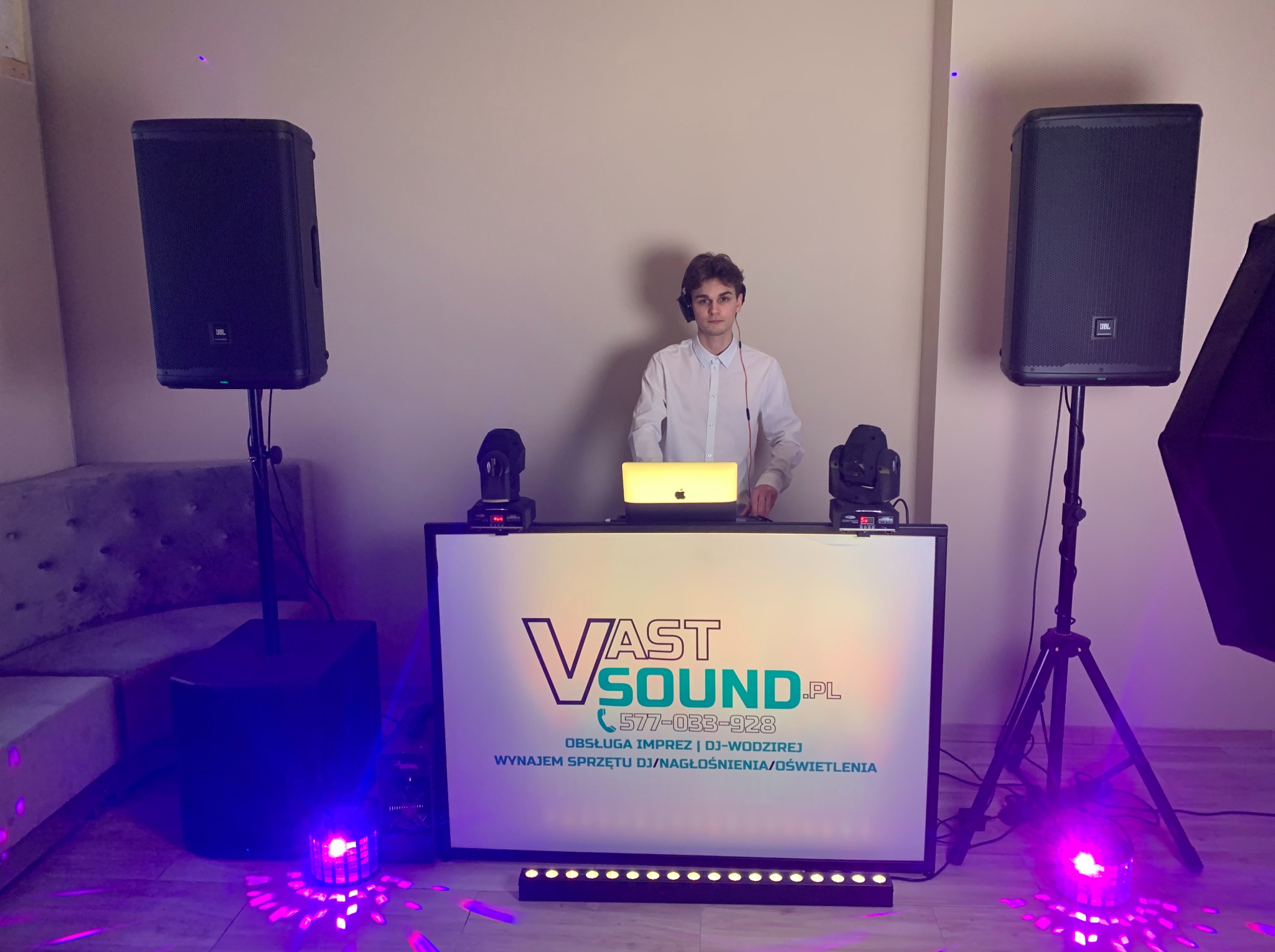 DJ VastSound za konsoletą z logo firmy, nagłośnienie JBL na statywach, oświetlenie sceniczne z efektami fioletowymi, laptop na blacie.
