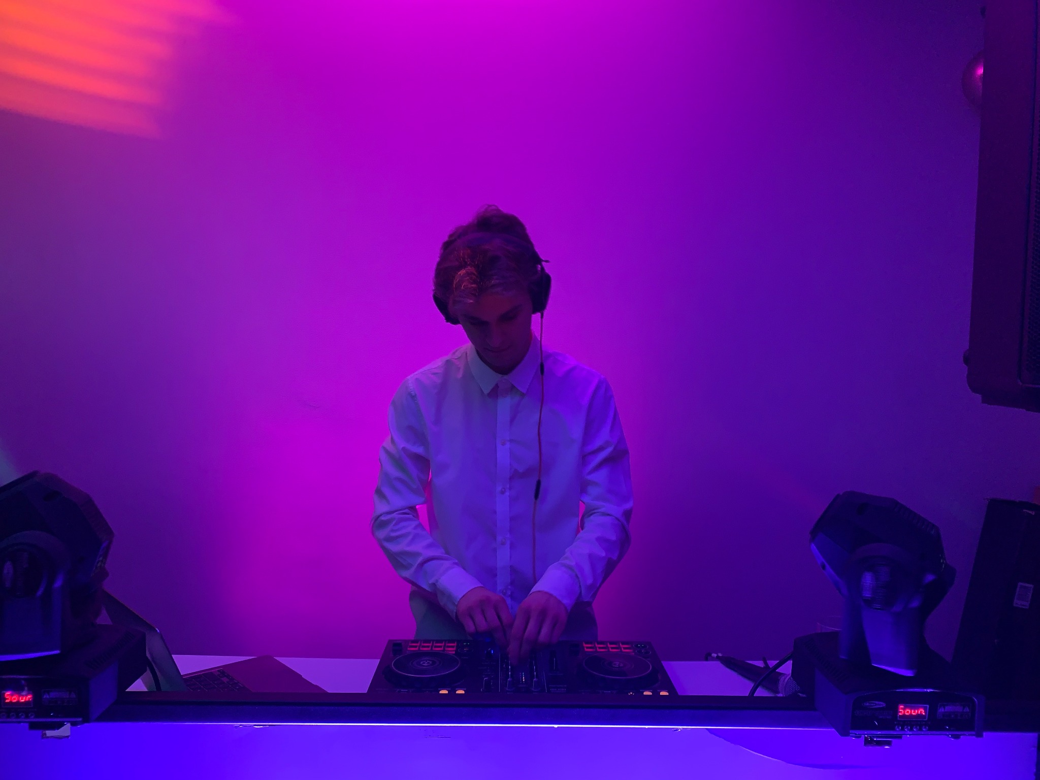 DJ w białej koszuli skupiony na miksowaniu muzyki na profesjonalnym sprzęcie, oświetlony fioletowym światłem podczas imprezy.