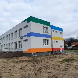 Nowo pomalowany, dwukondygnacyjny budynek z białymi ścianami i kolorowymi pasami (zielony, niebieski, żółty, pomarańczowy, czerwony) pod oknami, widok z zewnątrz na tle pochmurnego nieba i innych...