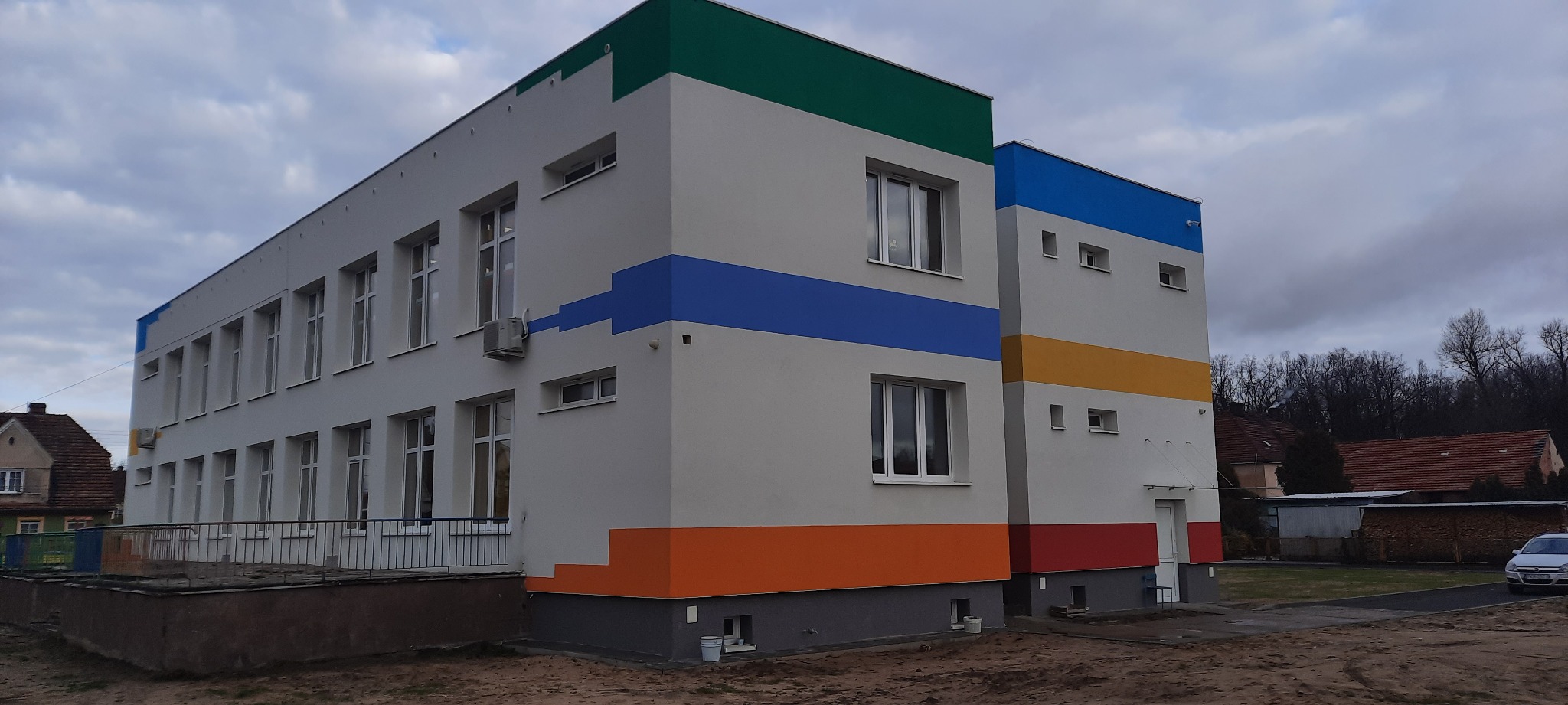 Odnowiony budynek szkoły z nowymi oknami PCV, pomalowany w jaskrawe kolory - zielony, niebieski, pomarańczowy i czerwony, widoczne klimatyzatory na elewacji.