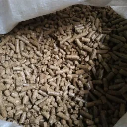 Wnętrze worka wypełnionego brązowymi, cylindrycznymi granulkami opału, widoczne z góry, z fragmentem białego worka w tle.