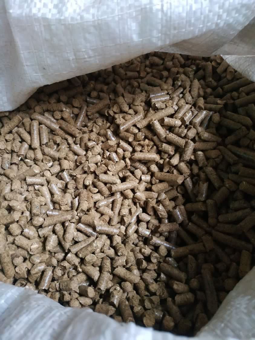 Wnętrze worka wypełnionego brązowymi, cylindrycznymi granulkami opału, widoczne z góry, z fragmentem białego worka w tle.