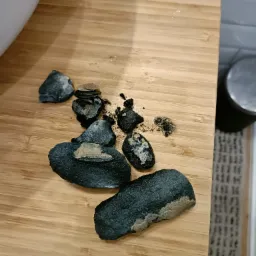 Fragmenty zanieczyszczeń usuniętych z rury, leżące na drewnianej desce, z widocznymi resztkami i osadami.