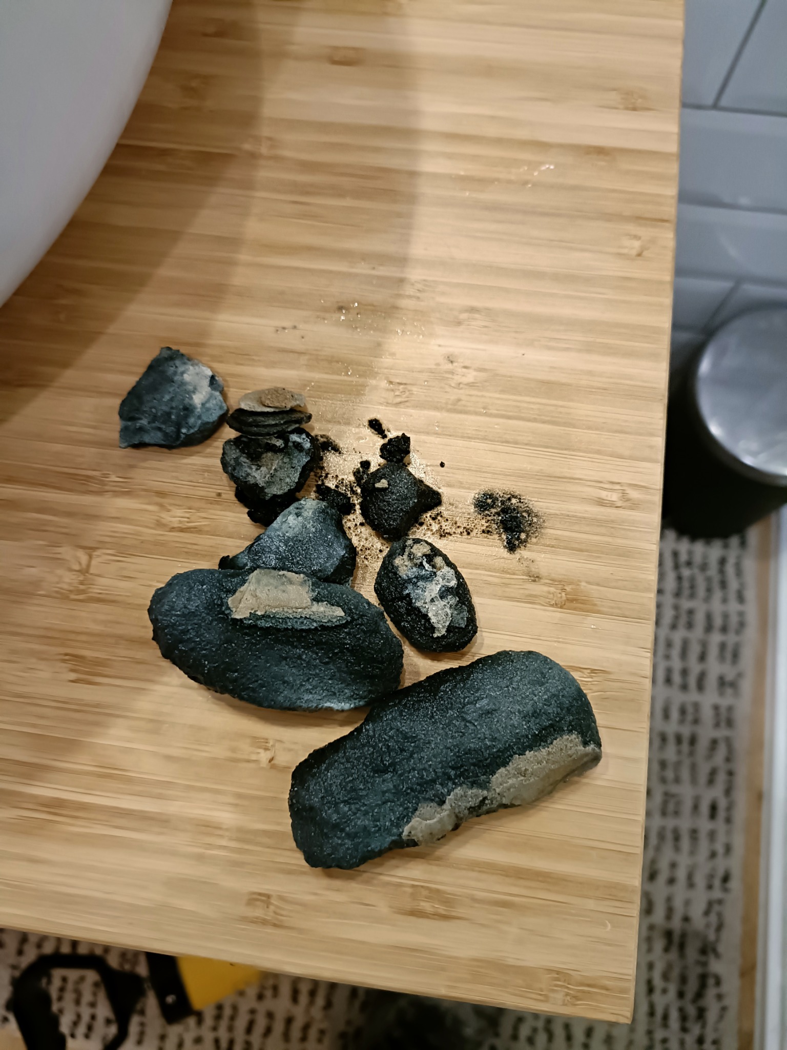 Fragmenty zanieczyszczeń usuniętych z rury, leżące na drewnianej desce, z widocznymi resztkami i osadami.