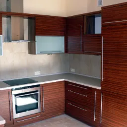 Nowoczesna kuchnia z fornirem w odcieniach brązu, jasny blat, zabudowa pod sufit, piekarnik w zabudowie, płyta indukcyjna i okap.