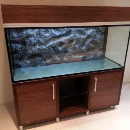 Pusty, nowoczesny akwarium z drewnianą obudową w kolorze orzecha, z tłem imitującym skały, umieszczone na szafce z dwojgiem drzwi i otwartą półką pośrodku.