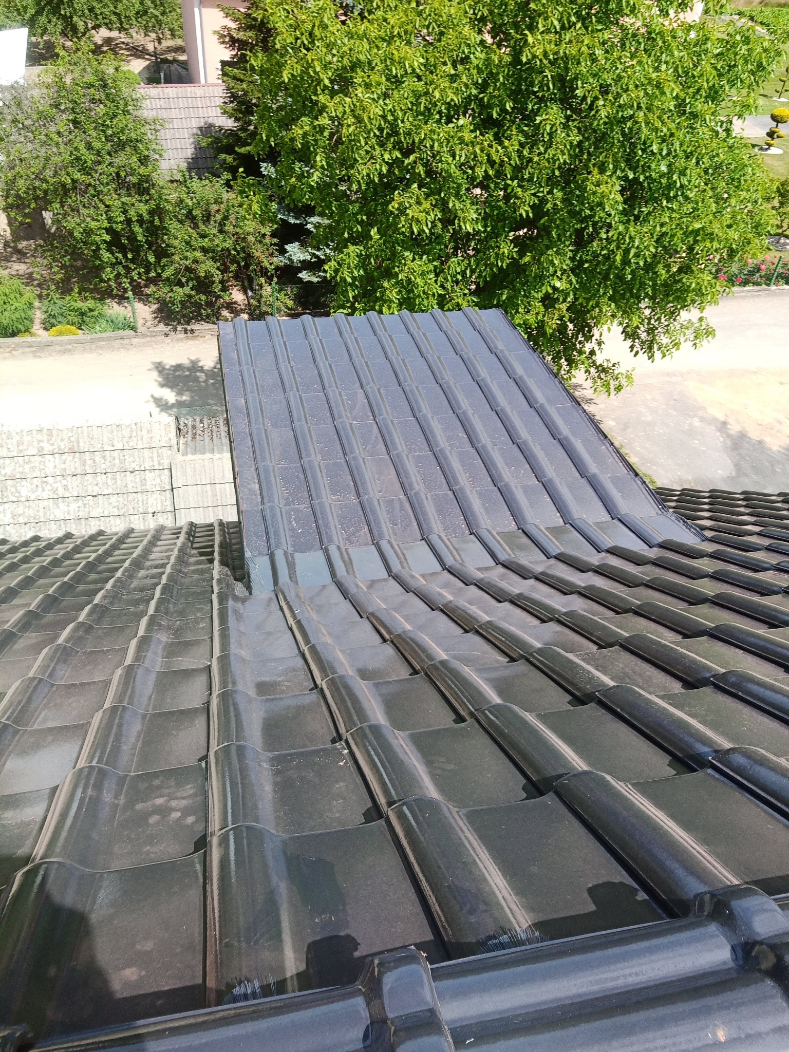 Fragment dachu z czarnej dachówki ceramicznej, widok z góry na łączenie nowej i starej części połaci.