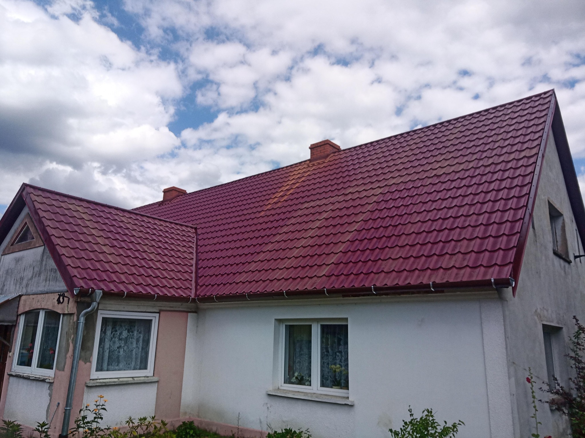 Dom jednorodzinny z nowym, bordowym dachem z blachodachówki, widok z dołu na tle pochmurnego nieba.