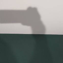 Pro-rem uslugi remontowe - Świeżo pomalowana, ciemnozielona ściana w dolnej części kadru, z widocznym cieniem dłoni trzymającej telefon w górnej części, rzucanym na białą ścianę.