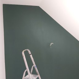 Pro-rem uslugi remontowe - Świeżo pomalowana, ciemnozielona ściana ze skosem, z widoczną drabinką malarską i wystającym kablem elektrycznym.