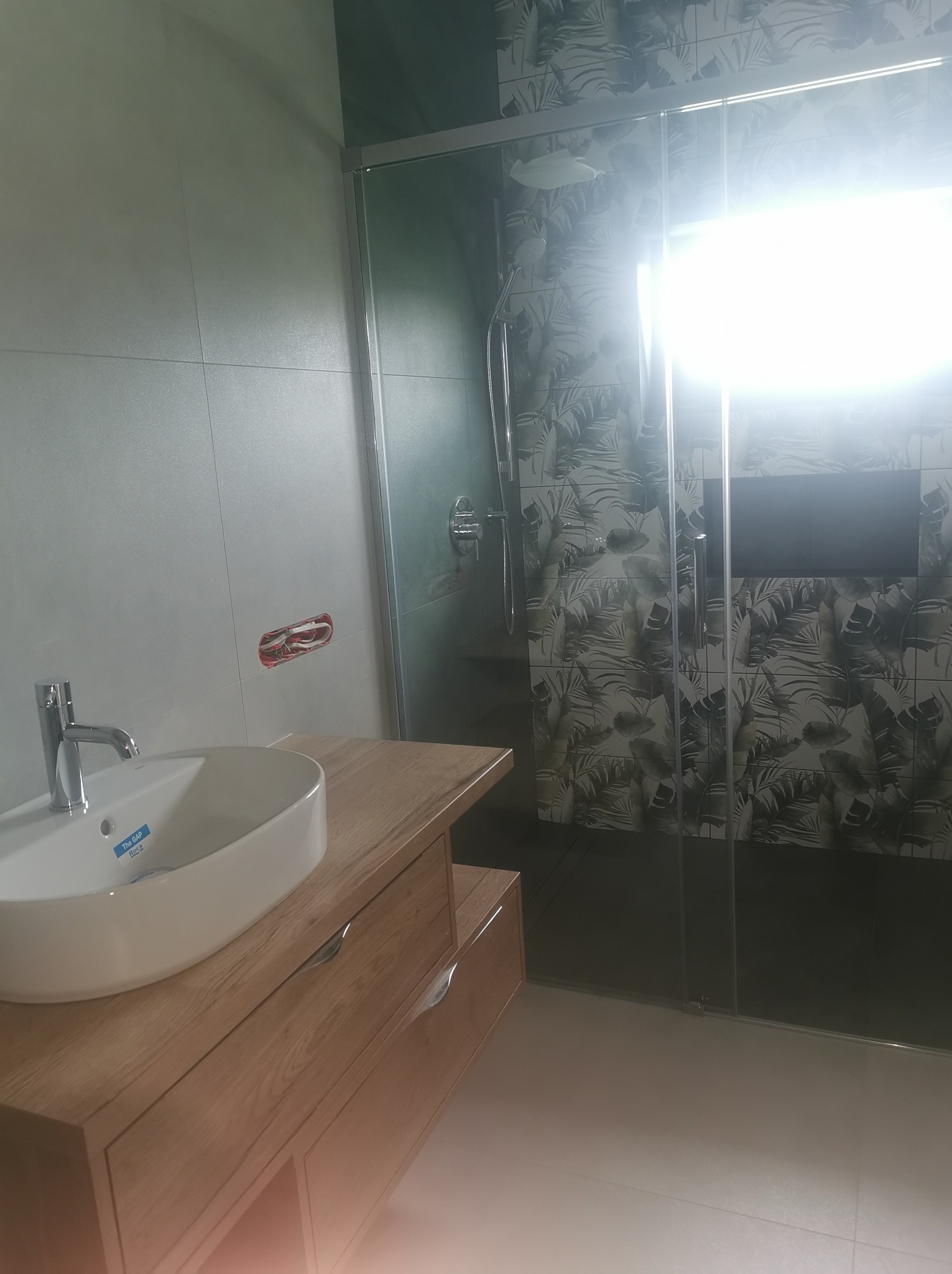 Nowoczesna łazienka w Łodzi z umywalką nablatową na drewnianej szafce i kabiną prysznicową ze szklanymi drzwiami oraz płytkami w tropikalne liście.