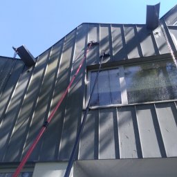 SOLARCELL - Metalowy dach i okno podczas czyszczenia za pomocą szczotek na długich tyczkach; widoczne krople wody i refleksy na szybie.