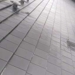 SOLARCELL - Częściowo umyty, ciemnoszary dach z dachówki ceramicznej z czterema odpowietrznikami, widoczny fragment lancy myjącej w lewym dolnym rogu.
