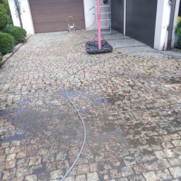 SOLARCELL - Mokry fragment kostki brukowej po czyszczeniu, widoczne różnice w kolorze między czystą a brudną powierzchnią, w tle garaże i drabina z żółtą szmatką.