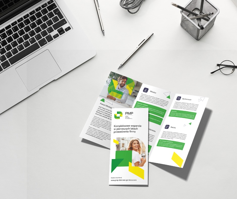 Rozłożona, trójdzielna ulotka reklamowa na białym biurku obok laptopa, długopisów i okularów, prezentująca ofertę firmy PMP dla młodych przedsiębiorstw, z zielono-żółtą grafiką.