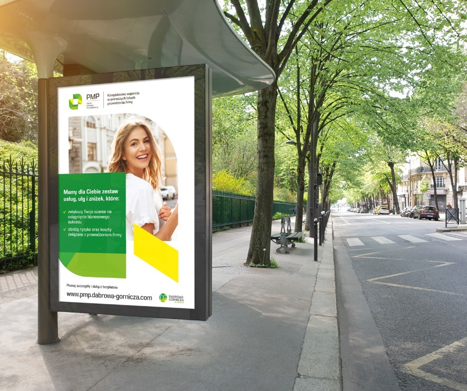 Przystanek autobusowy z reklamą firmy PMP oferującej wsparcie dla nowych firm, na plakacie uśmiechnięta kobieta na tle budynku.