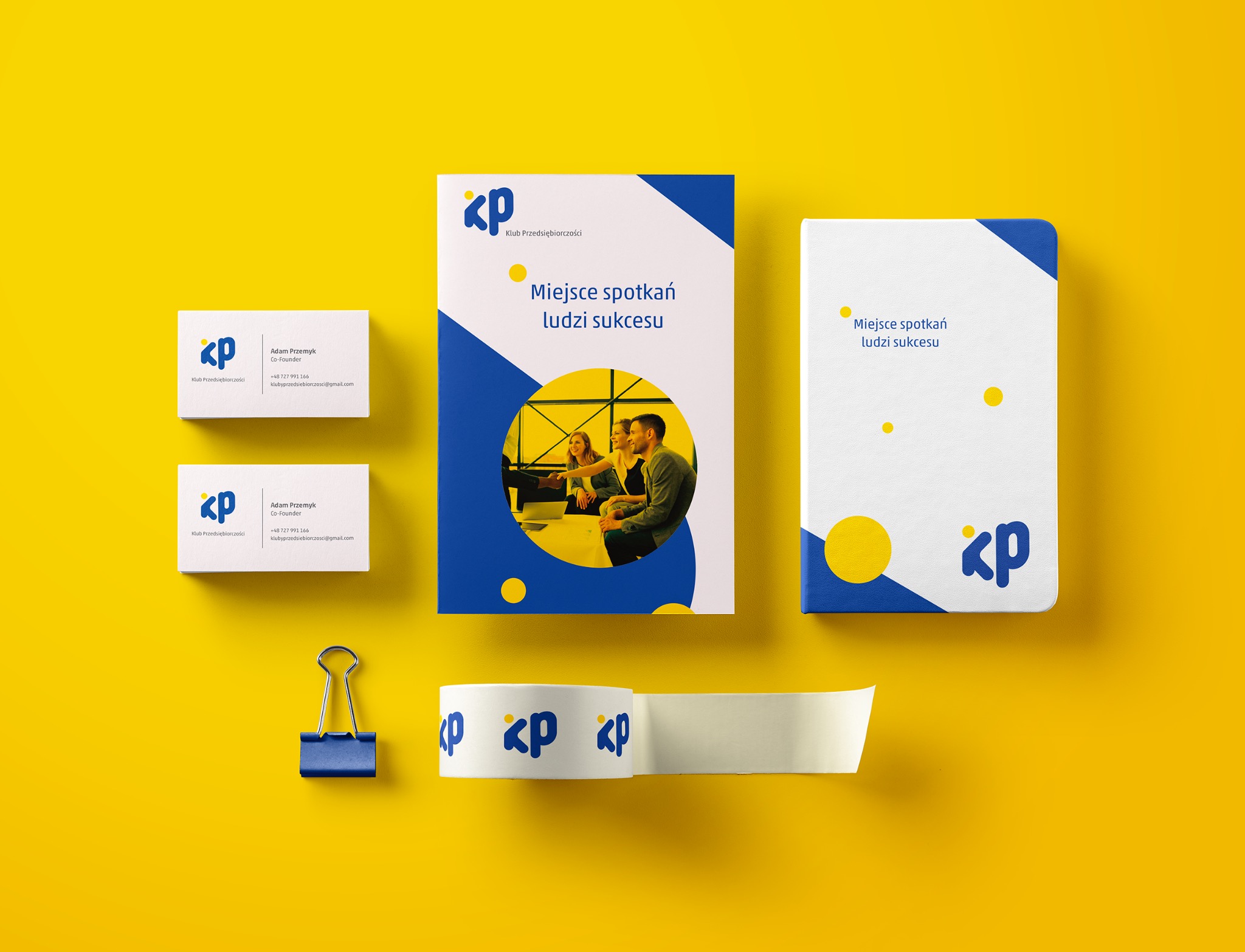 Mockup materiałów firmowych na żółtym tle: wizytówki z danymi kontaktowymi, broszura z hasłem 'Miejsce spotkań ludzi sukcesu', notes i taśma klejąca z logo firmy.