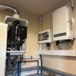 Wnętrze kotłowni z piecem gazowym, rozdzielnicą elektryczną i inwerterem fotowoltaicznym SolarEdge. Widoczne rury instalacji CO i CWU.