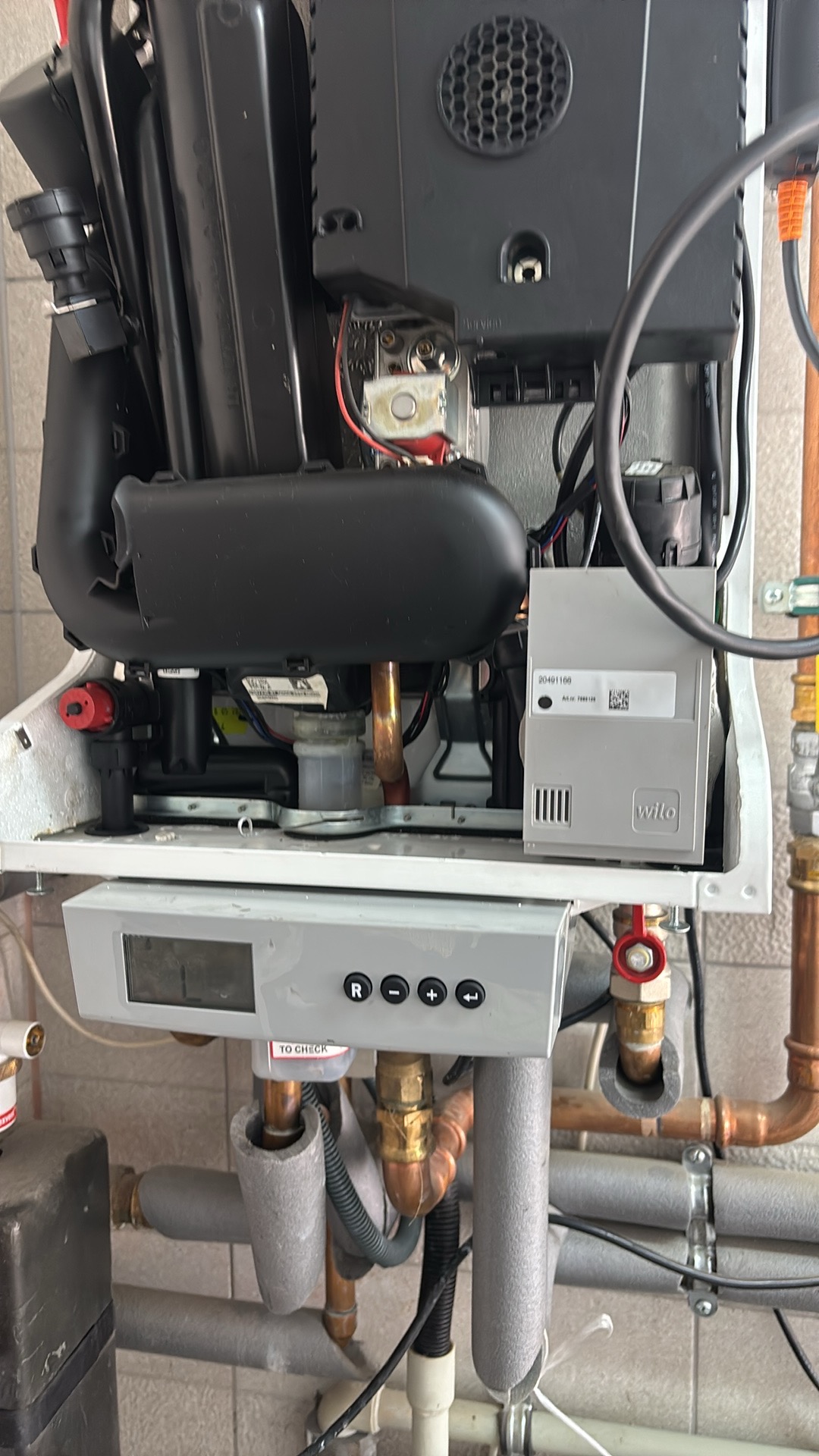 Otwarty piec gazowy z widocznymi elementami wewnętrznymi, miedzianymi rurami i szarym sterownikiem Wilo. Widoczne przyłącza i przewody.