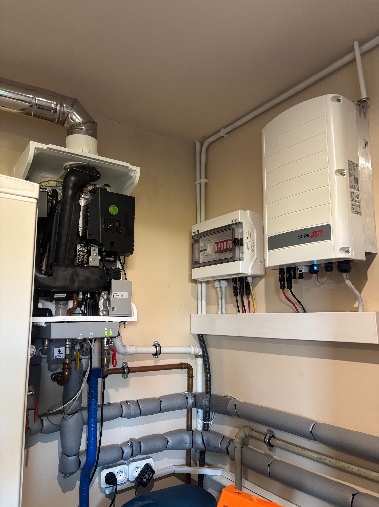 Wnętrze kotłowni z piecem gazowym, rozdzielnicą elektryczną i inwerterem fotowoltaicznym SolarEdge. Widoczne rury instalacji CO i CWU.