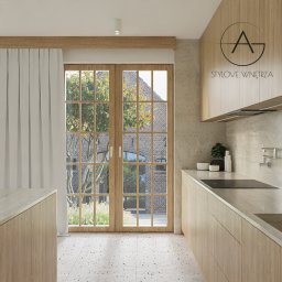 STYLOVE WNĘTRZA - Jasna kuchnia z drewnianymi frontami i oknem z widokiem na ceglany budynek. Minimalistyczny design, kamienny blat, designerska bateria ścienna, logo firmy na szafce.