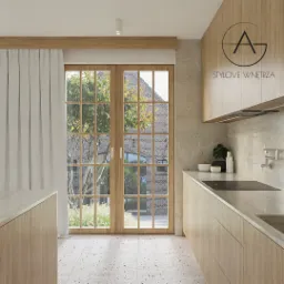 Jasna kuchnia z drewnianymi frontami i oknem z widokiem na ceglany budynek. Minimalistyczny design, kamienny blat, designerska bateria ścienna, logo firmy na szafce.