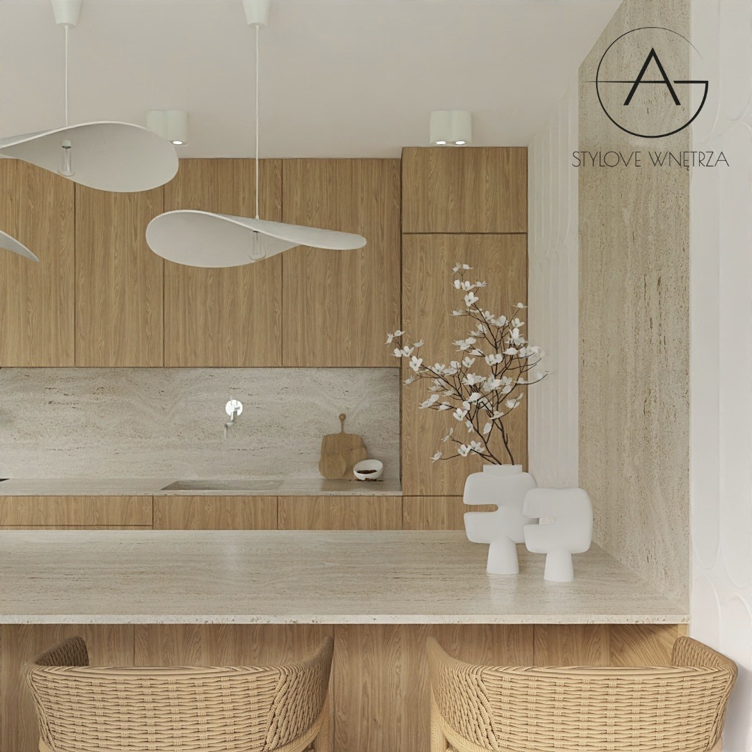 Jasna kuchnia z drewnianymi szafkami i blatem z kamienia naturalnego, oświetlona wiszącymi lampami w kształcie kapeluszy, z dekoracyjnym wazonem z kwitnącymi gałązkami i dwoma plecionymi krzesłami...