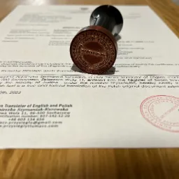 Dokument poświadczony pieczęcią tłumacza przysięgłego, leżący na drewnianym biurku, z widocznym stemplem i podpisem.