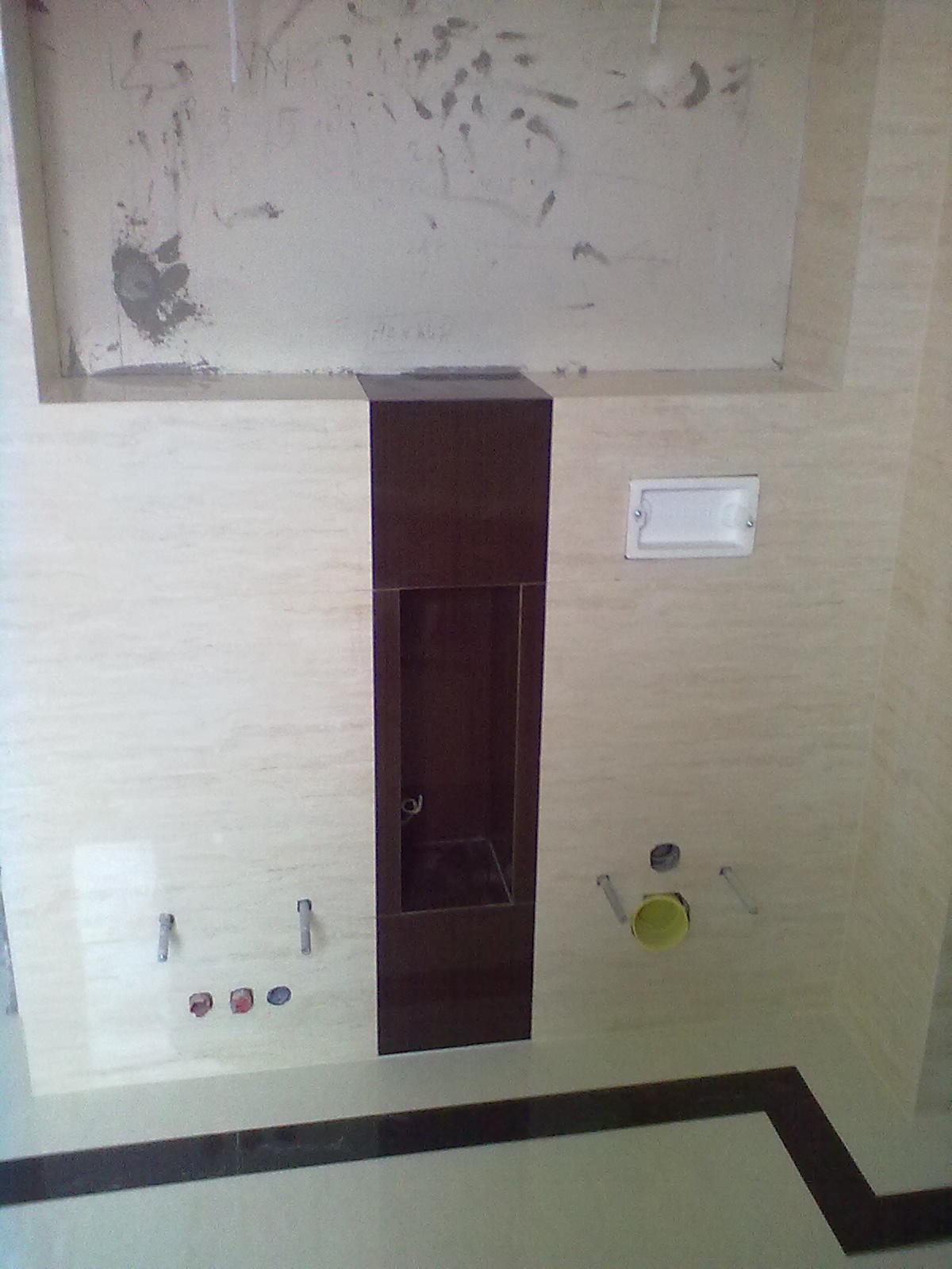 Ściana łazienki z beżowymi płytkami imitującymi marmur, z wnęką wykończoną ciemnobrązowymi płytkami, widoczne instalacje wodne i elektryczne przed montażem armatury.