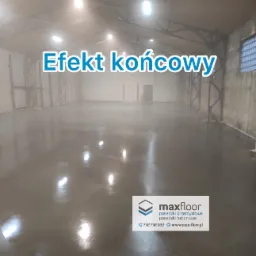 Błyszcząca, gładka posadzka w hali przemysłowej, widoczne odbicia świateł, surowy beton na ścianach, w tle metalowa konstrukcja dachu.