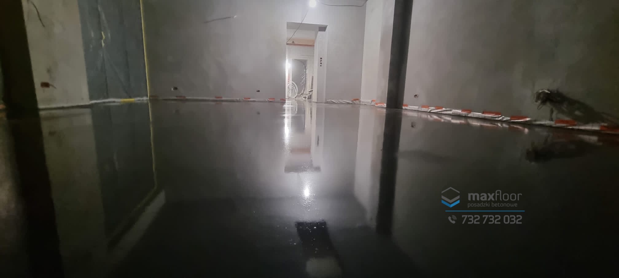 Świeżo wylana, błyszcząca posadzka przemysłowa z widocznymi elementami instalacji ogrzewania podłogowego w surowym wnętrzu, z logo firmy Maxfloor w prawym dolnym rogu.