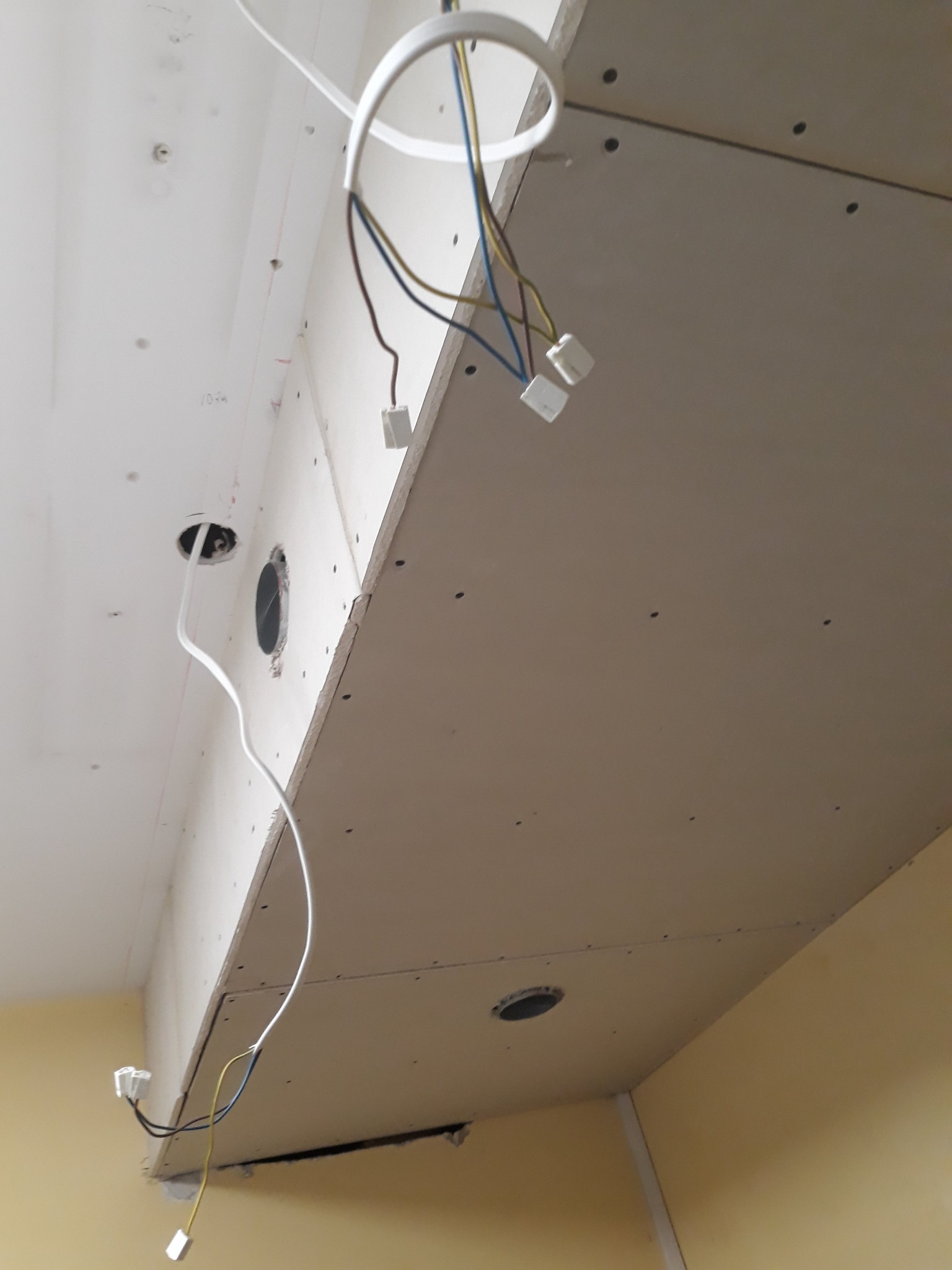 Montaż sufitu podwieszanego z płyt gipsowo-kartonowych, widoczne przewody elektryczne i otwory na oświetlenie.